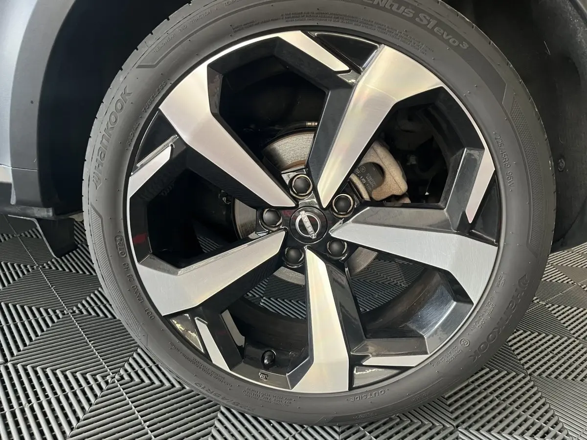 Gros plan sur la jante alliage bicolore noir et argent du Nissan Juke Hybrid 2024 gris clair, vue côté droit.