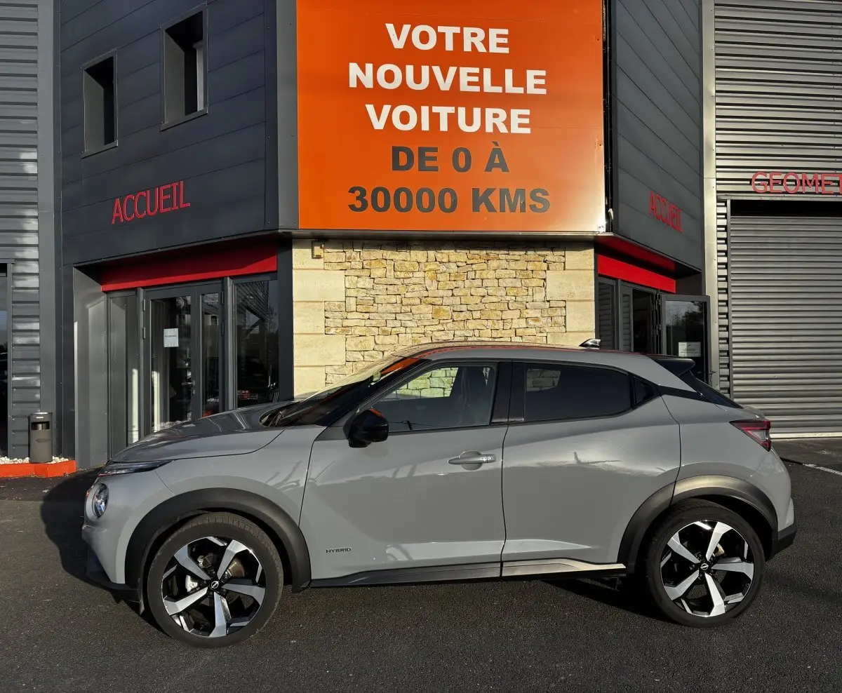 Profil droit d'un Nissan Juke Hybrid gris clair 2024 avec jantes noires et détails noirs contrastants.