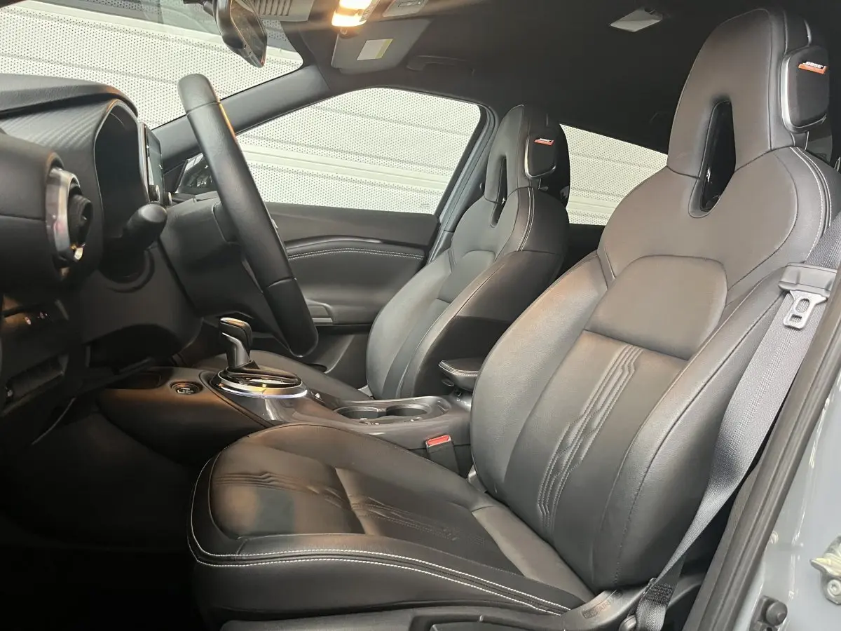 Vue intérieure côté conducteur du Nissan Juke Hybrid 143 Tekna cuir, sièges sport noirs avec surpiqûres blanches.