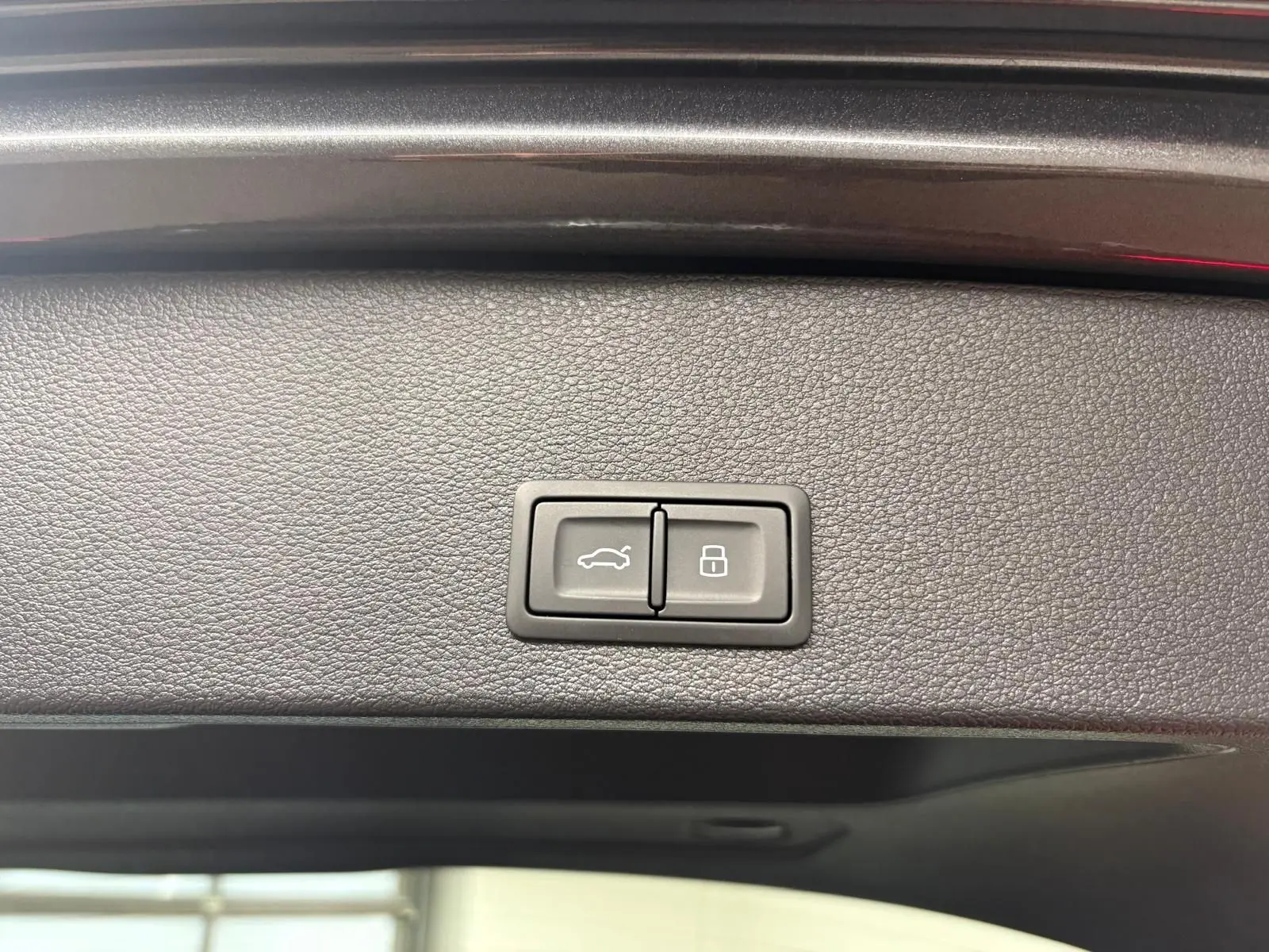 Boutons de commande du hayon électrique et de verrouillage intégrés sur la garniture intérieure du coffre d'un Audi Q2 gris Daytona.