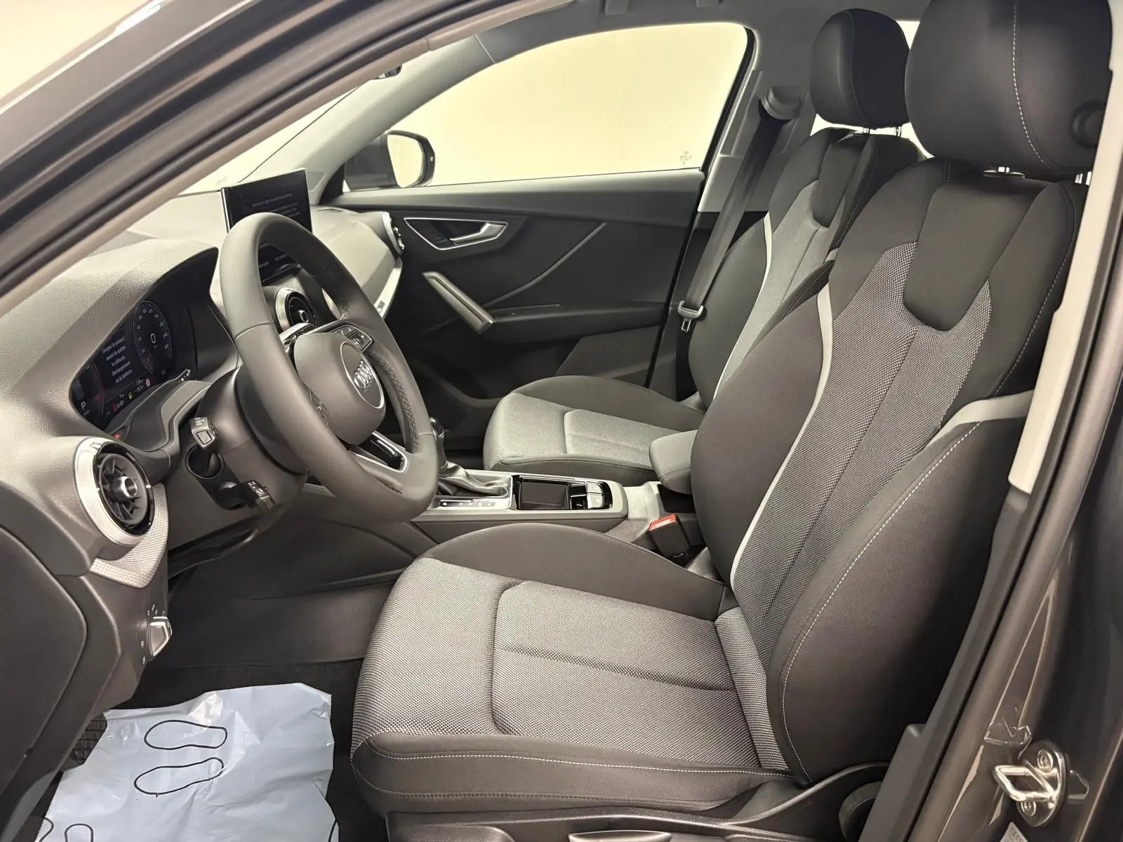 Vue intérieure côté gauche de l'Audi Q2 35 TFSI S Line 2026, sièges tissu gris et tableau de bord moderne.