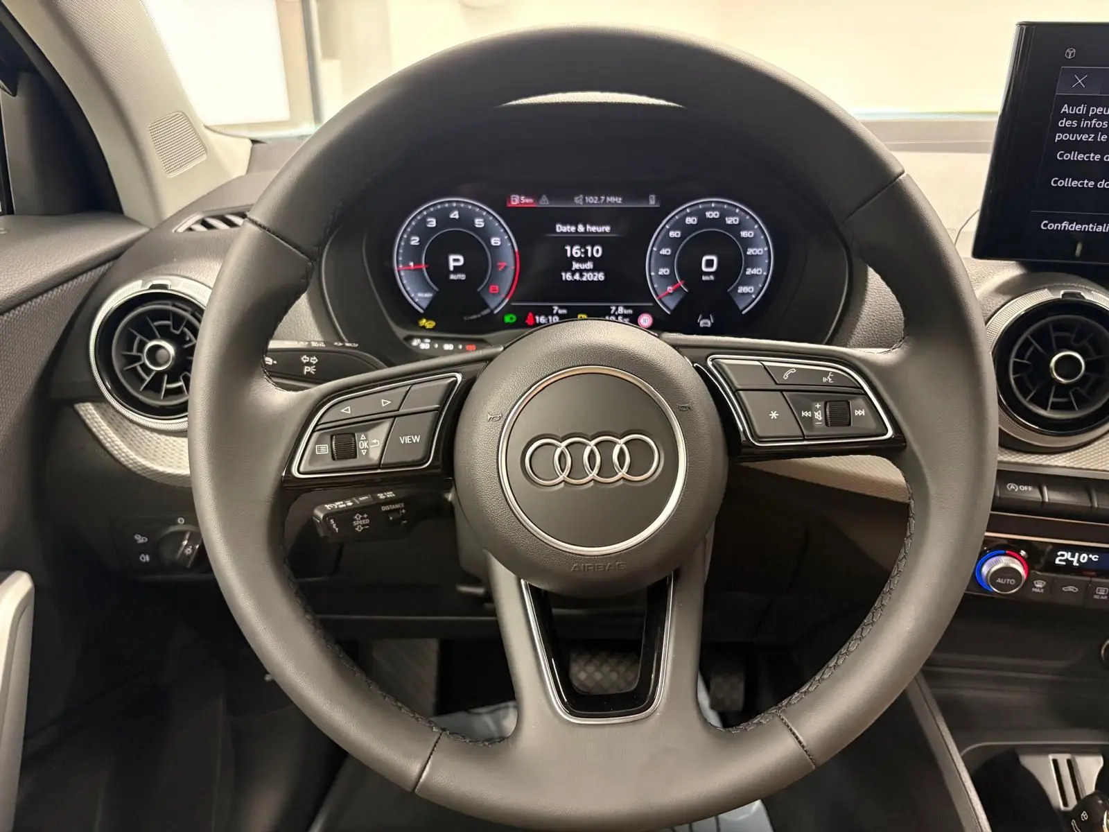 Vue intérieure centrée sur le volant noir de l'Audi Q2 35 TFSI 150 S Line avec tableau de bord numérique allumé.