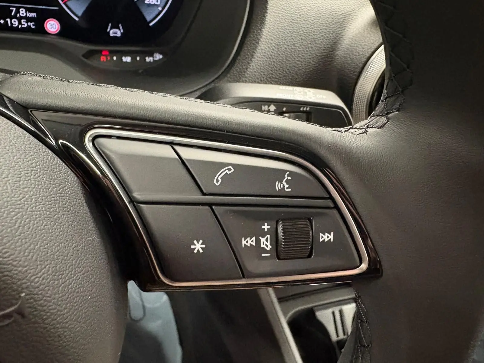 Gros plan sur les commandes multifonctions au volant de l'Audi Q2 35 TFSI S Line gris Daytona, tableau de bord en arrière-plan.