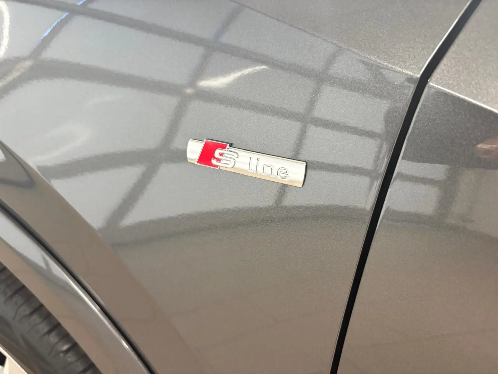 Gros plan sur l'écusson S line sur l'aile avant droite d'un Audi Q2 gris Daytona métallisé.