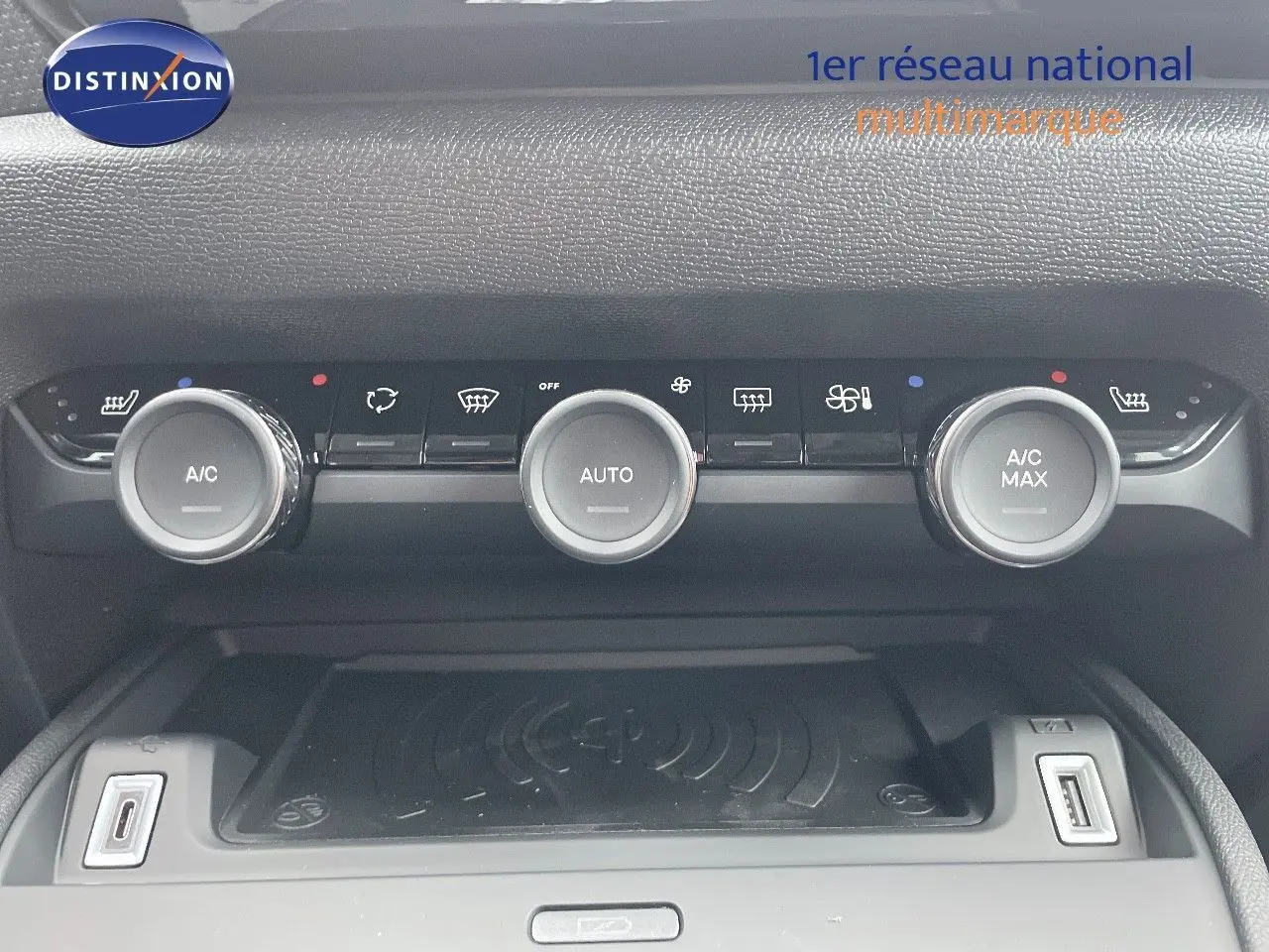 Vue rapprochée de la console centrale de la Citroën C4 blanche, montrant les commandes de climatisation et un chargeur sans fil.