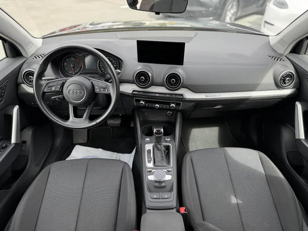 Intérieur Audi Q2 2022 vu de face, tableau de bord gris avec volant cuir noir et console centrale moderne.