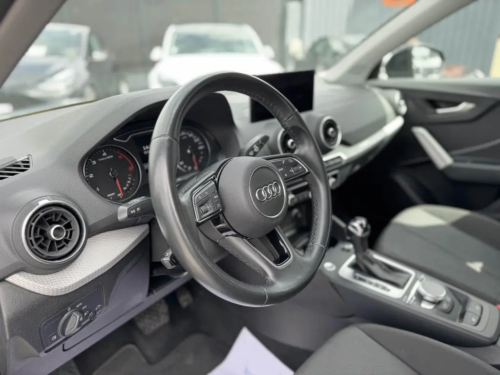 Intérieur noir d'Audi Q2 2022 vu côté conducteur, volant cuir multifonction et console centrale avec boîte auto.