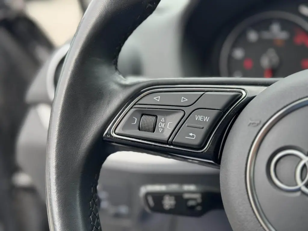 Gros plan sur les commandes gauche du volant cuir noir de l'Audi Q2 2022 avec boutons multifonctions et molette.