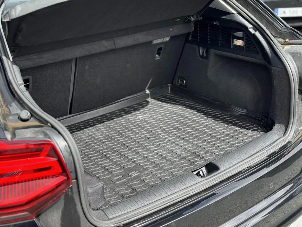 Coffre ouvert vu de l'arrière gauche d'un Audi Q2 noir avec tapis de coffre en caoutchouc et feux arrière LED rouges.