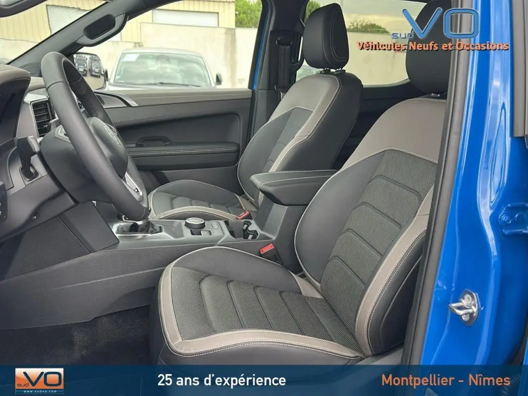 Intérieur côté gauche du Volkswagen Amarok Aventura bleu 2025, montrant sièges cuir gris avec accoudoir central et volant multifonctions.