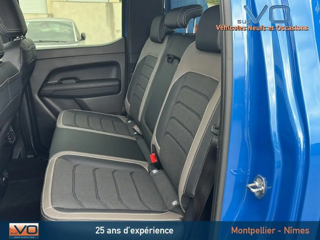 Vue latérale des sièges arrière en cuir noir et gris du Volkswagen Amarok Simple Cabine bleu 2025, avec porte ouverte.