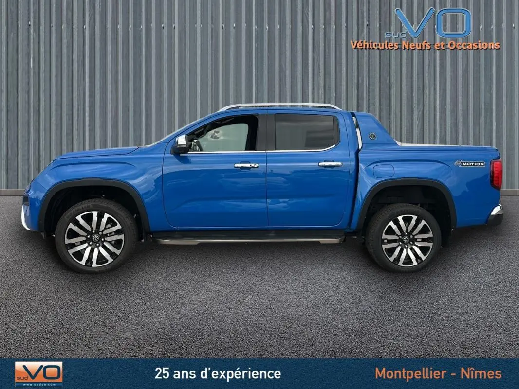 Profil côté gauche du pick-up Volkswagen Amarok Aventura bleu 2025 avec jantes alliage 21 pouces et marchepieds visibles.