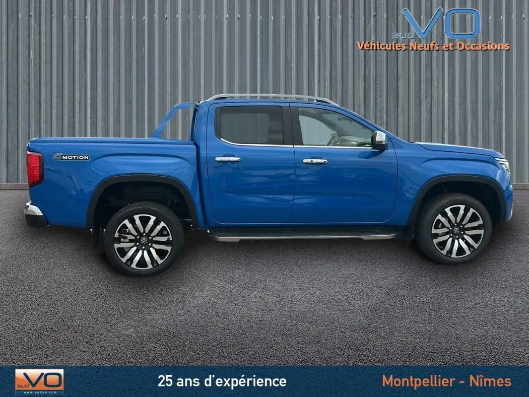 Profil côté gauche du pick-up Volkswagen Amarok bleu 2025 avec jantes alliage 21 pouces et marchepieds visibles.