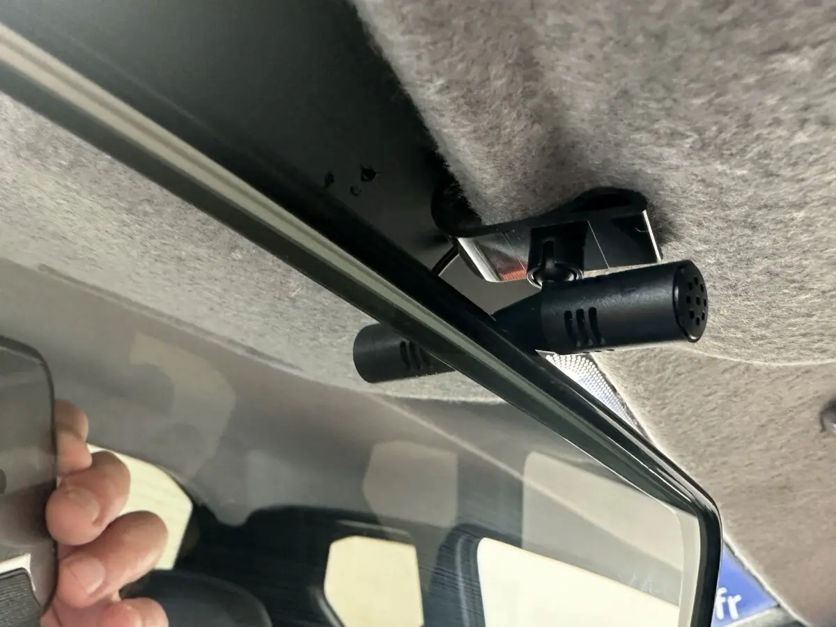 Gros plan intérieur sur la caméra fixée au plafond, au-dessus du rétroviseur d'une Aixam Ambition blanche.