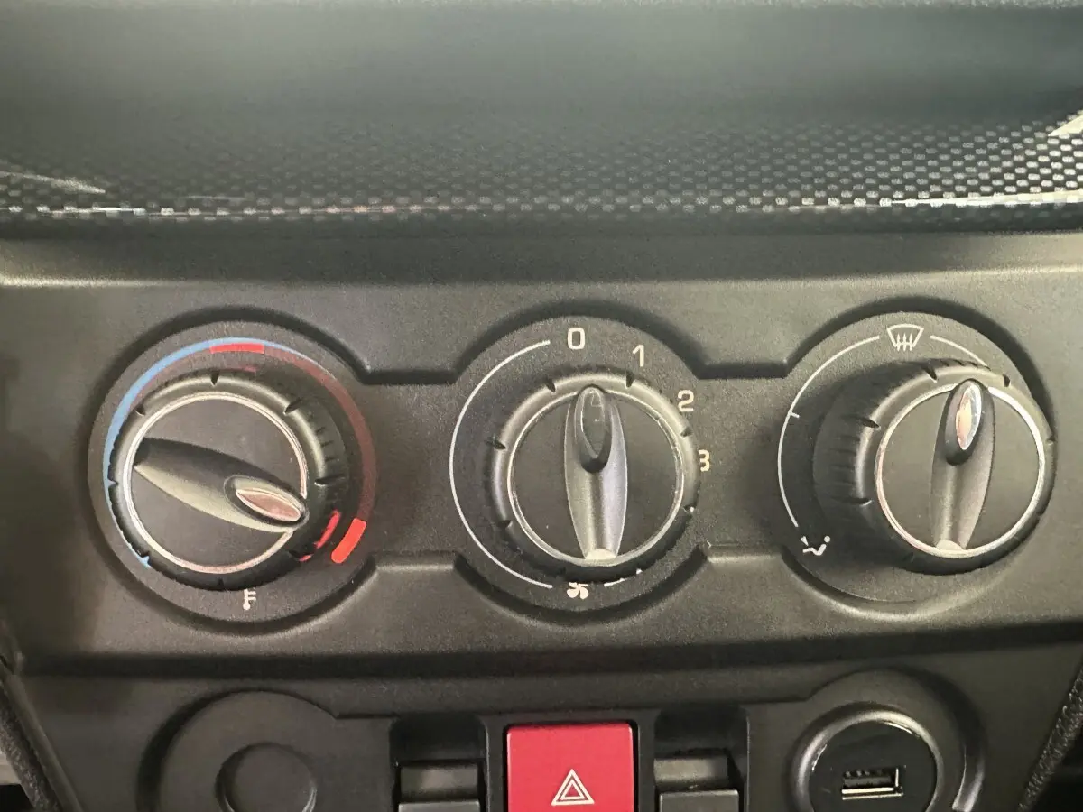 Gros plan sur les commandes de climatisation et bouton de signal d’urgence du tableau de bord d’une Aixam Ambition blanche.