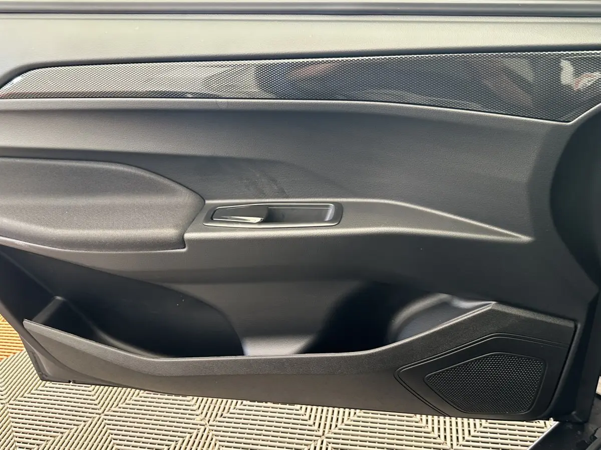 Vue intérieure du panneau de porte côté conducteur de l'AIXAM AMBITION 0.5 CITY GTO blanc avec poignée argentée et haut-parleur intégré.