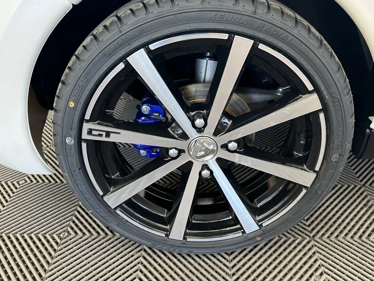 Gros plan sur la roue avant droite de l'AIXAM AMBITION 0.5 CITY GTO blanche, jante noire et argent avec logo GT.