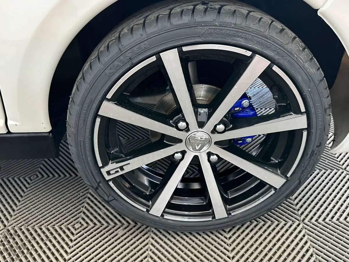 Gros plan sur la roue avant droite de l'AIXAM AMBITION 0.5 CITY GTO blanche avec jante noire et argentée et étrier de frein bleu.