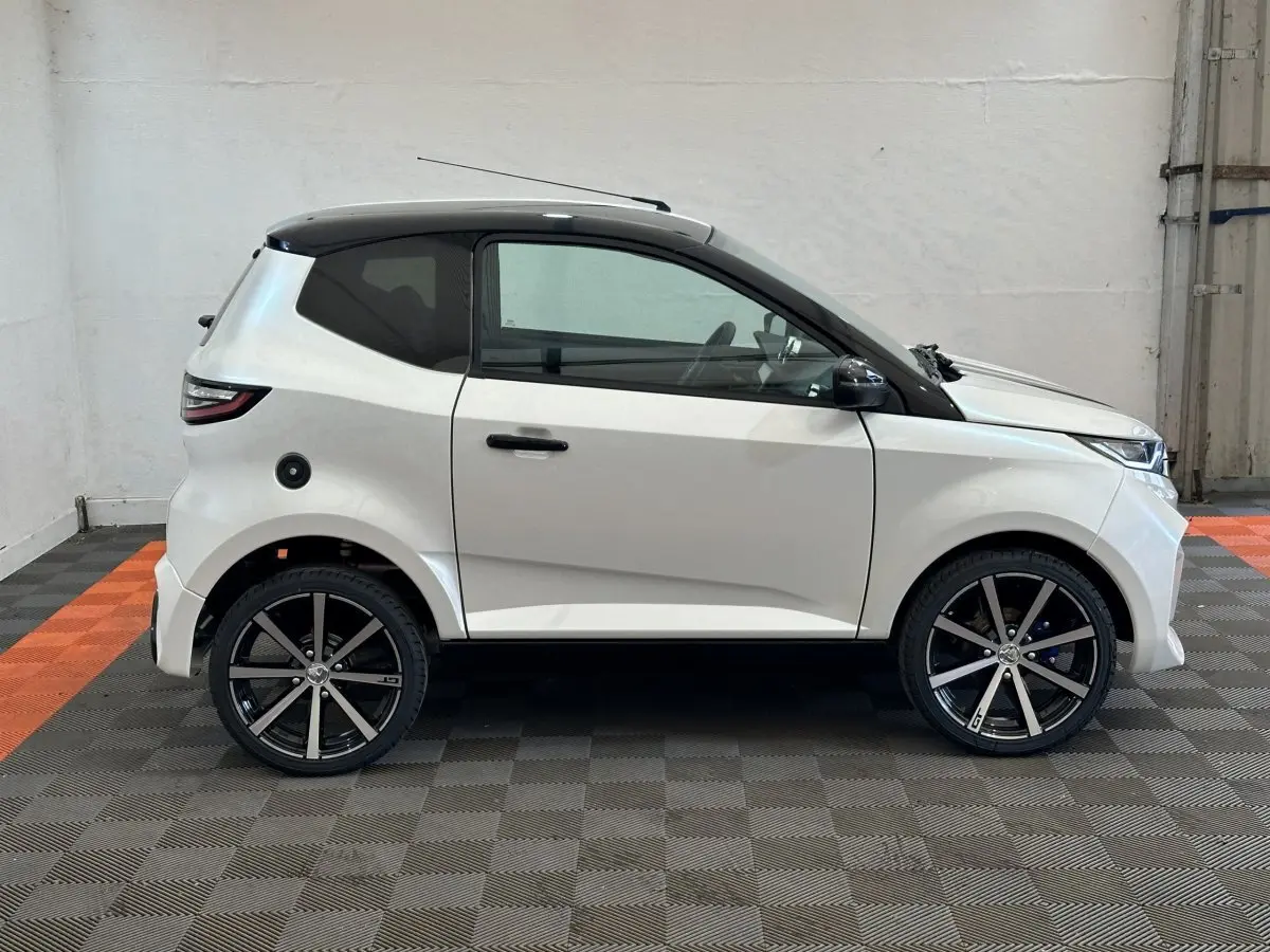 Vue de profil côté gauche d'une Aixam Ambition 0.5 City GTO blanche avec toit noir et jantes noires en intérieur.
