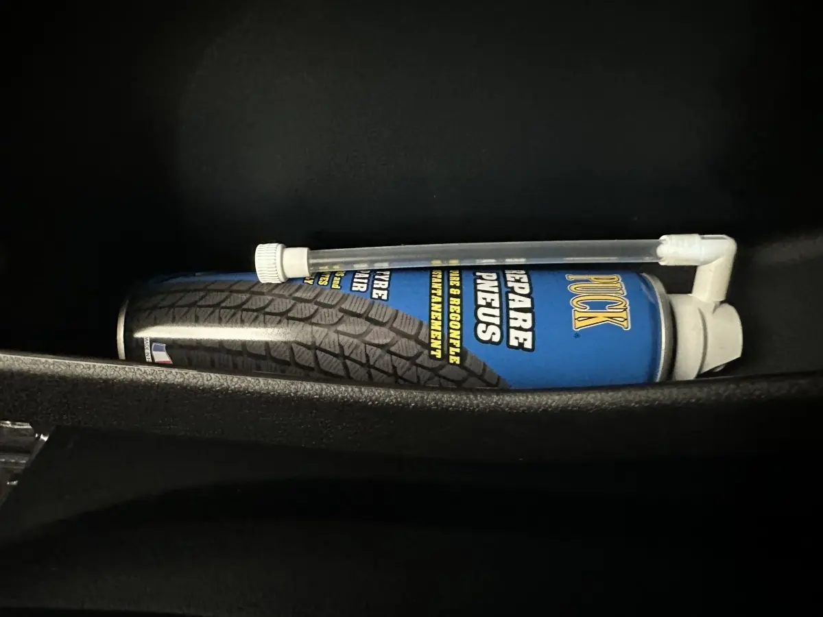 Image intérieure montrant une bombe de réparation pneus rangée dans le compartiment d'une Aixam Ambition 0.5 City GTO blanche.