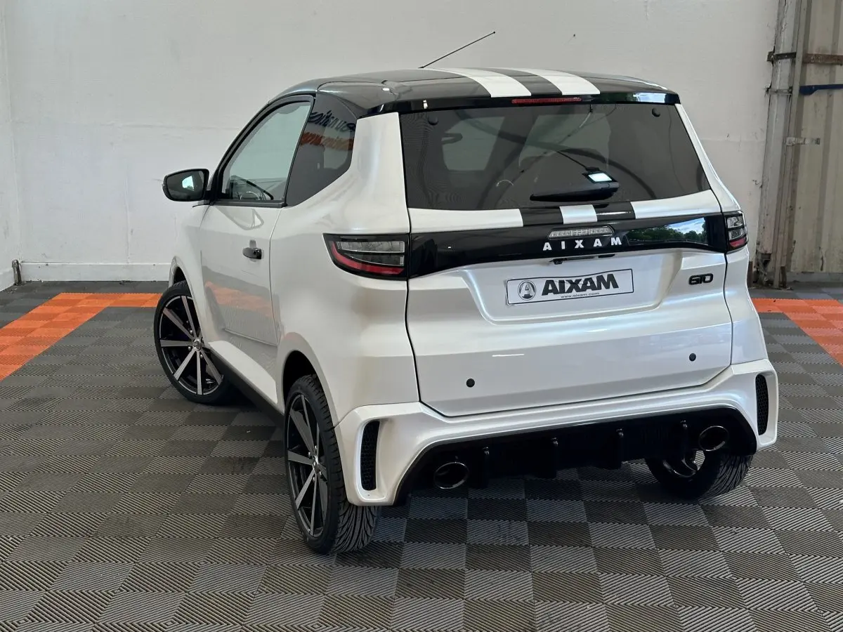 Vue 3/4 arrière droite de l'AIXAM AMBITION 0.5 CITY GTO blanc avec toit noir et bandes blanches, jantes noires, et caméra côté conducteur.