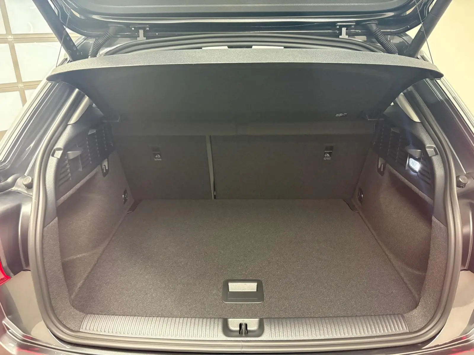 Coffre ouvert vu de l'arrière d'un Audi Q2 gris Daytona, montrant un espace de chargement propre et bien éclairé.