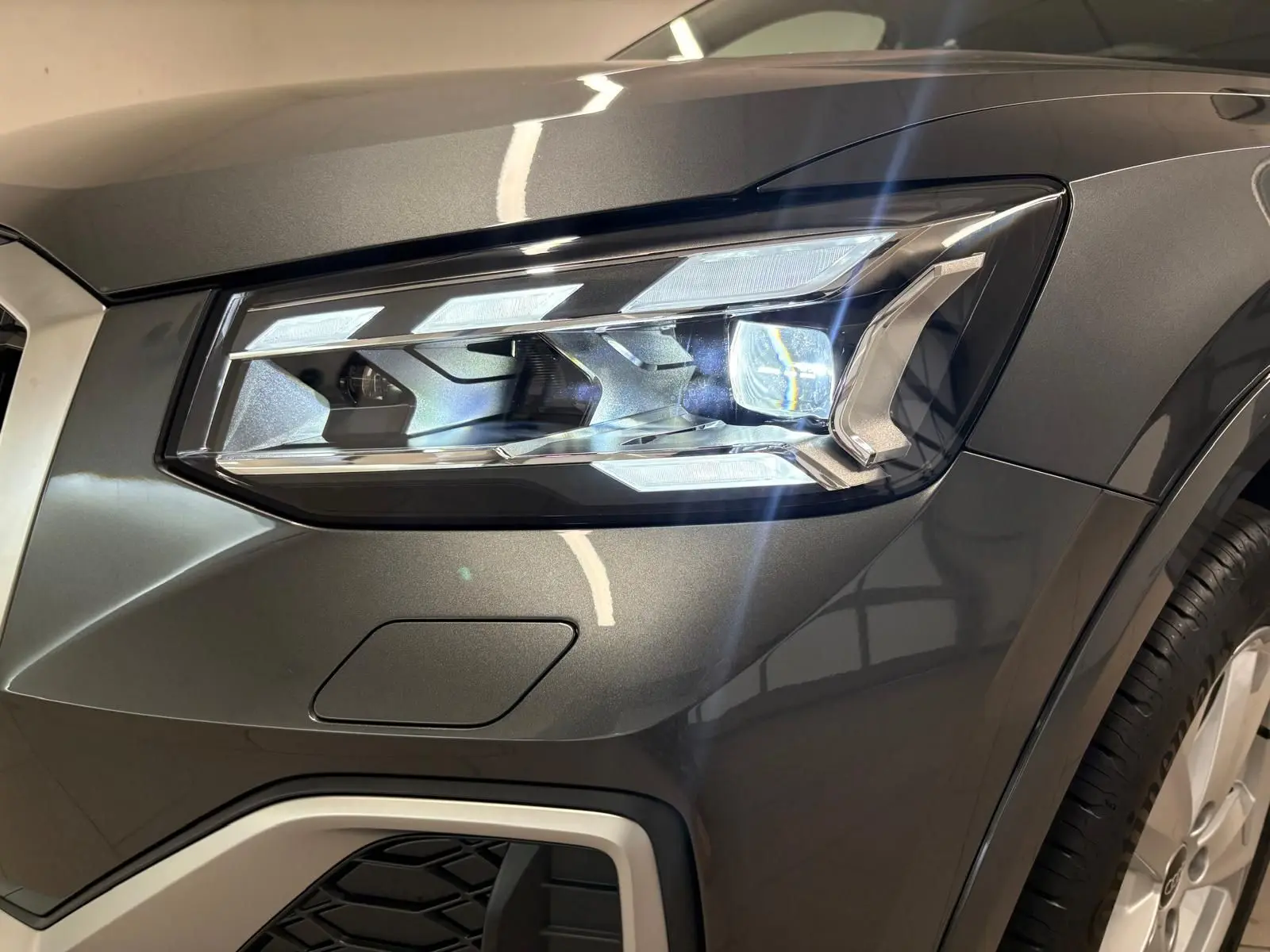 Gros plan sur le phare avant droit d’un Audi Q2 35 TFSI S Line gris Daytona métallisé, avec détails lumineux et carrosserie brillante.