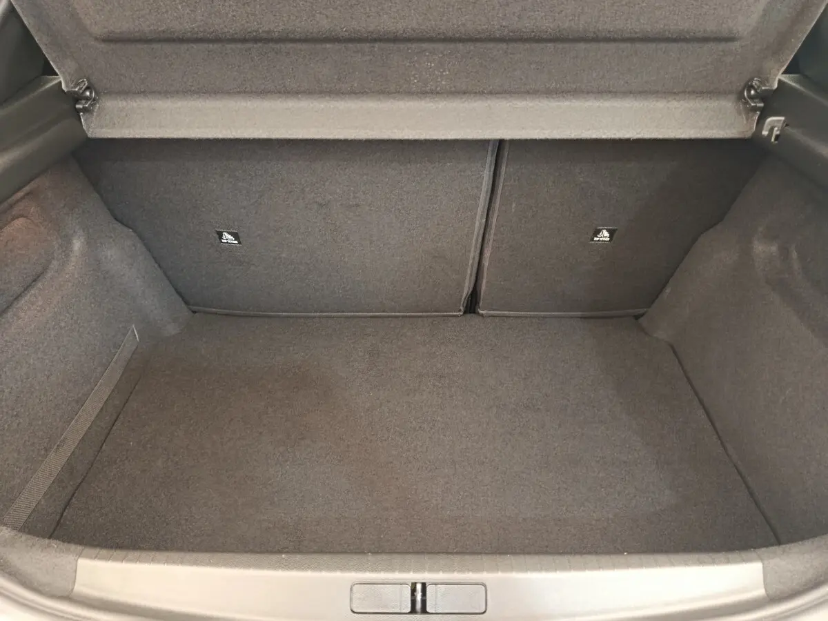 Coffre ouvert vu de face d'une Peugeot 208 blanche, espace de chargement vide et revêtement gris foncé.