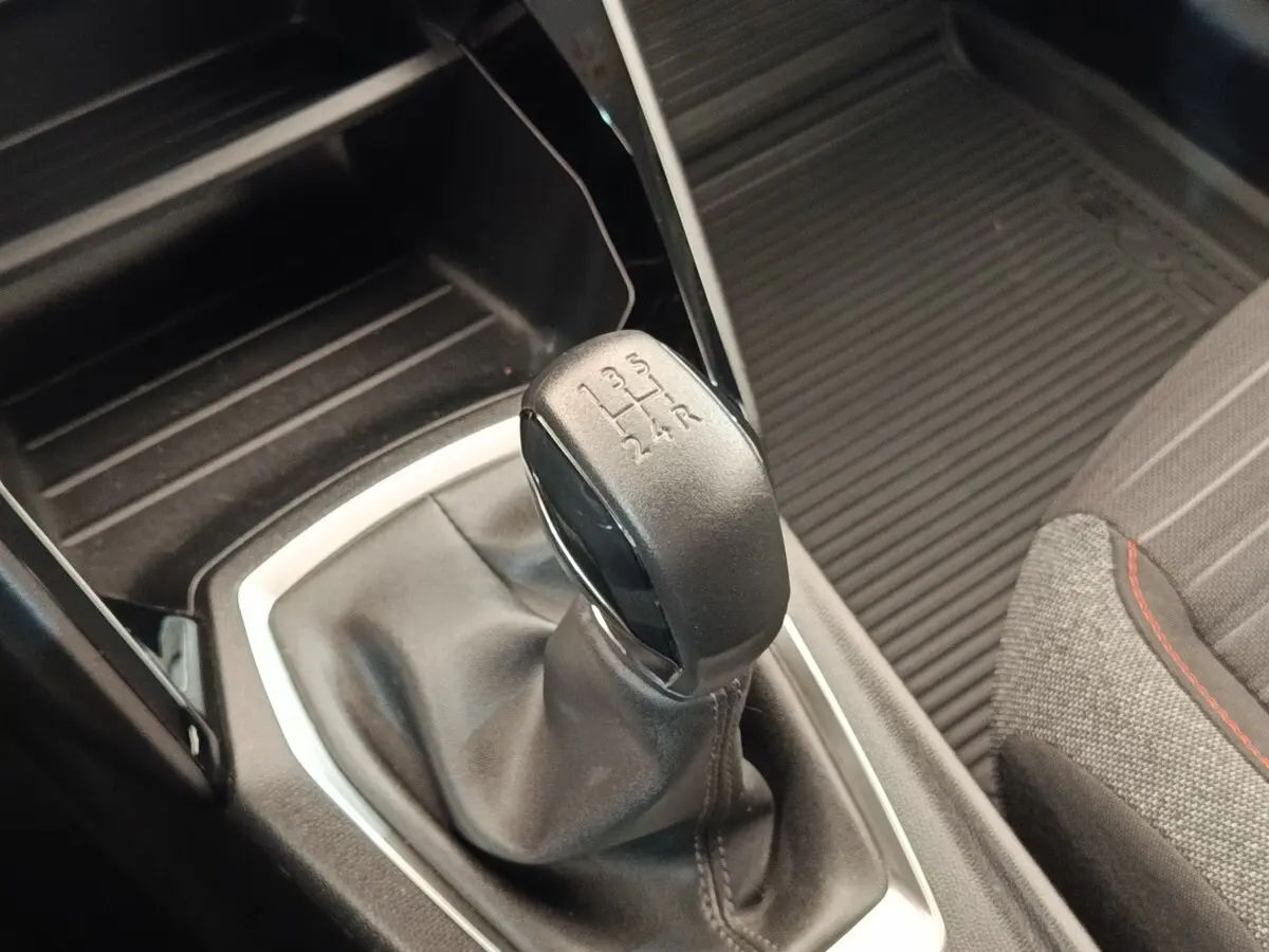 Gros plan sur le levier de vitesses manuel noir de la Peugeot 208 PureTech 75, avec partie tissu et coutures visibles.