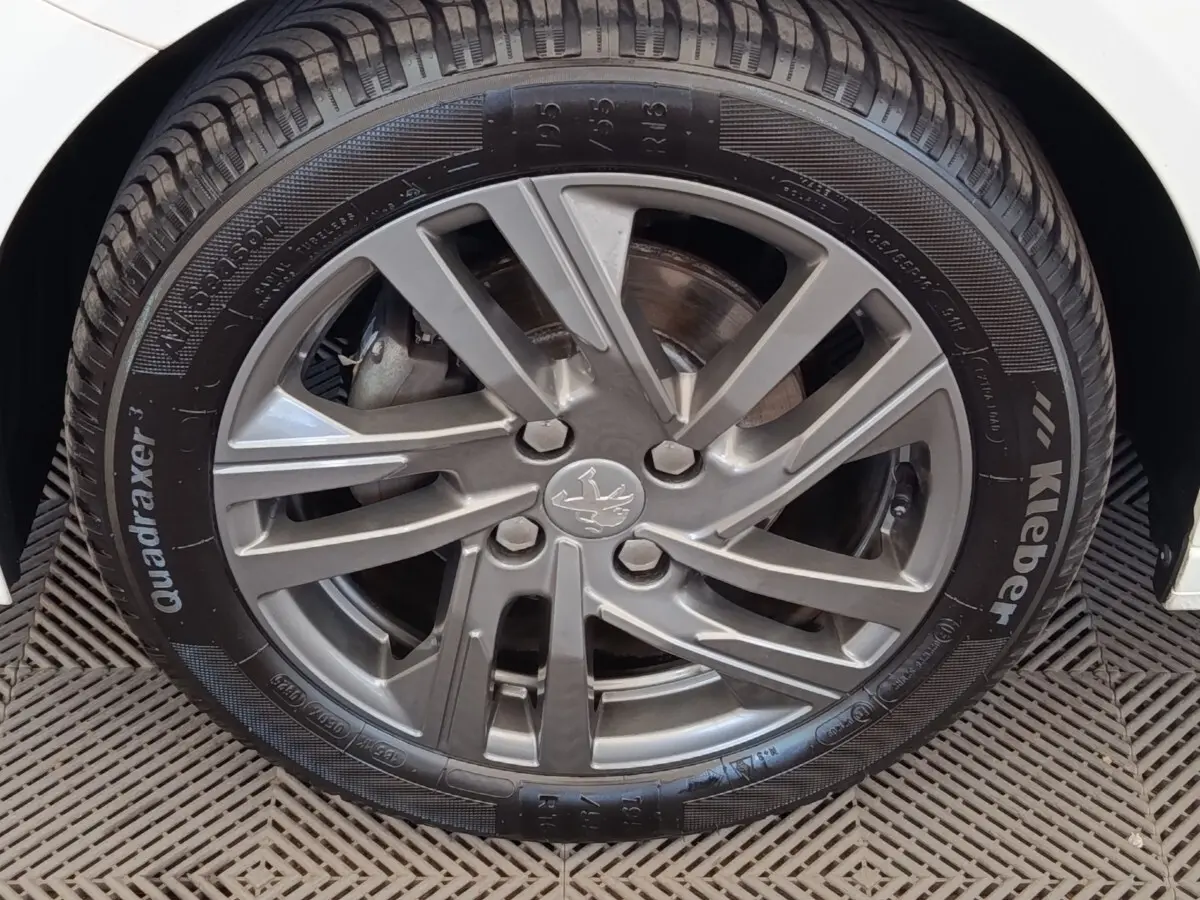Gros plan sur la roue avant droite d'une Peugeot 208 blanche, mettant en valeur la jante alliage grise et le pneu Kleber.