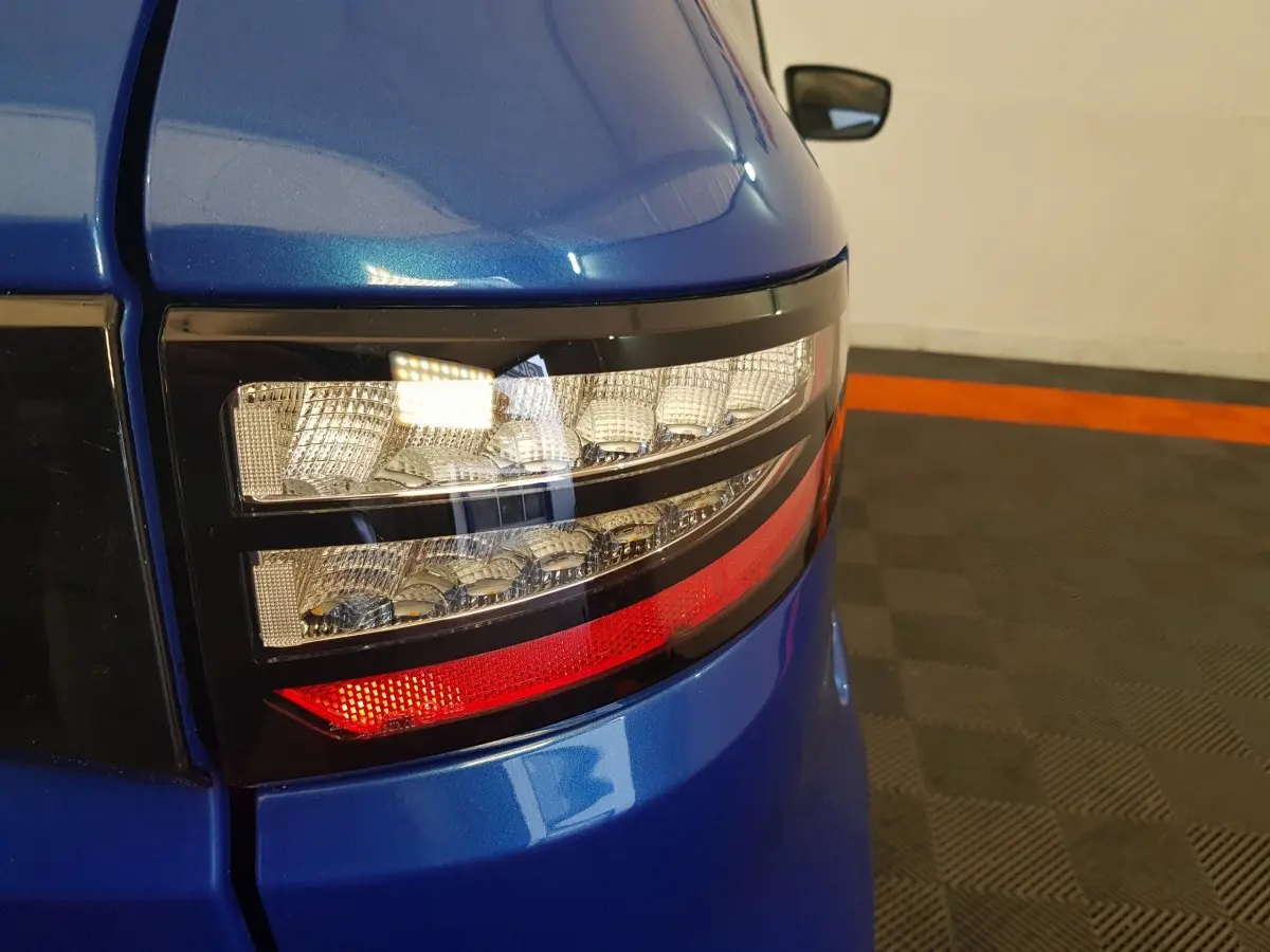 Gros plan sur le feu arrière droit bleu de l'AIXAM AMBITION 0.5 CITY SPORT avec rétroviseur caméra côté conducteur visible.