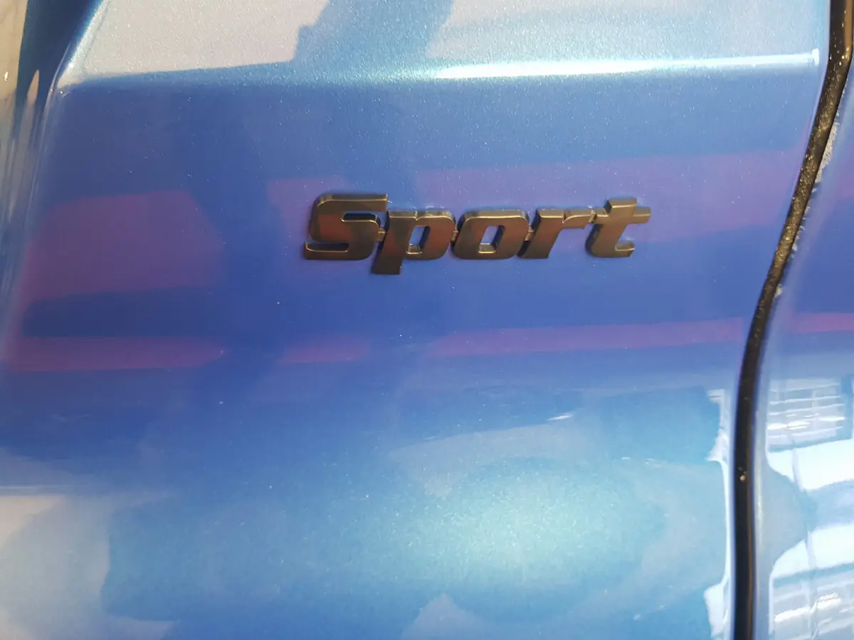 Gros plan sur l’inscription Sport en noir sur la carrosserie bleu métallisé de l’AIXAM AMBITION 0.5 CITY SPORT.