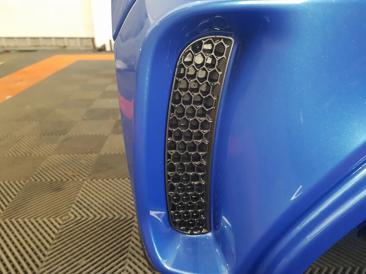 Gros plan sur la prise d'air noire en nid d'abeille du côté gauche de l'AIXAM AMBITION 0.5 CITY SPORT bleu.