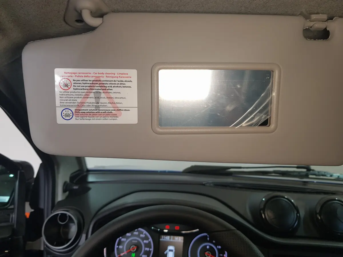 Vue intérieure centrée sur le pare-soleil côté conducteur avec miroir, tableau de bord noir et volant d'AIXAM Ambition bleu 2026.