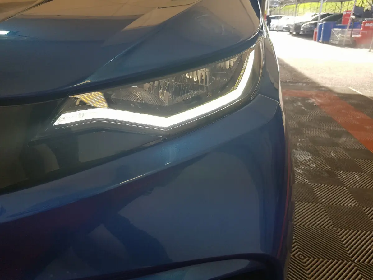 Gros plan sur le phare avant gauche allumé de l’AIXAM AMBITION 0.5 CITY SPORT bleu 2026, avec carrosserie brillante.