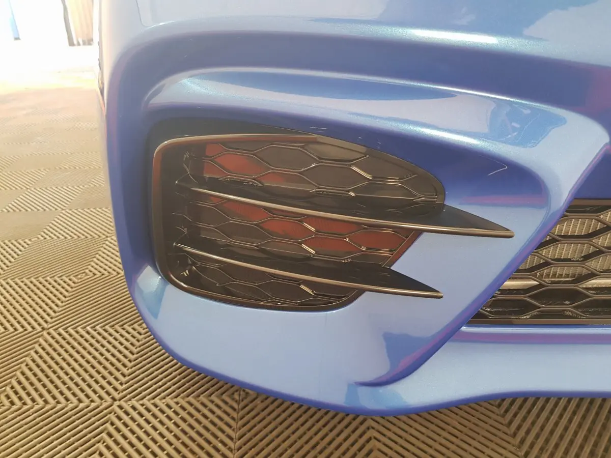 Gros plan sur la calandre avant droite bleu métallisé de l'AIXAM AMBITION 0.5 CITY SPORT avec grille noire alvéolée.