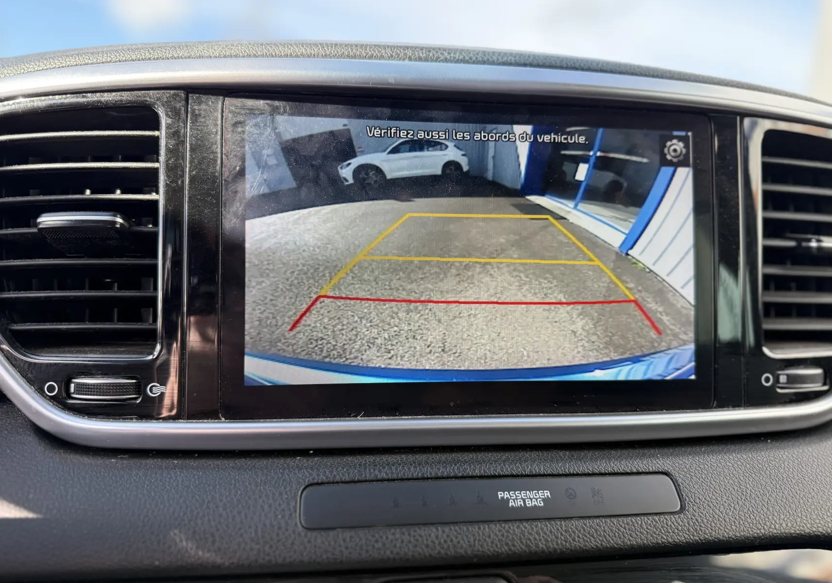 Écran central montrant la caméra de recul du Kia Sportage bleu, avec lignes de guidage en rouge et jaune.