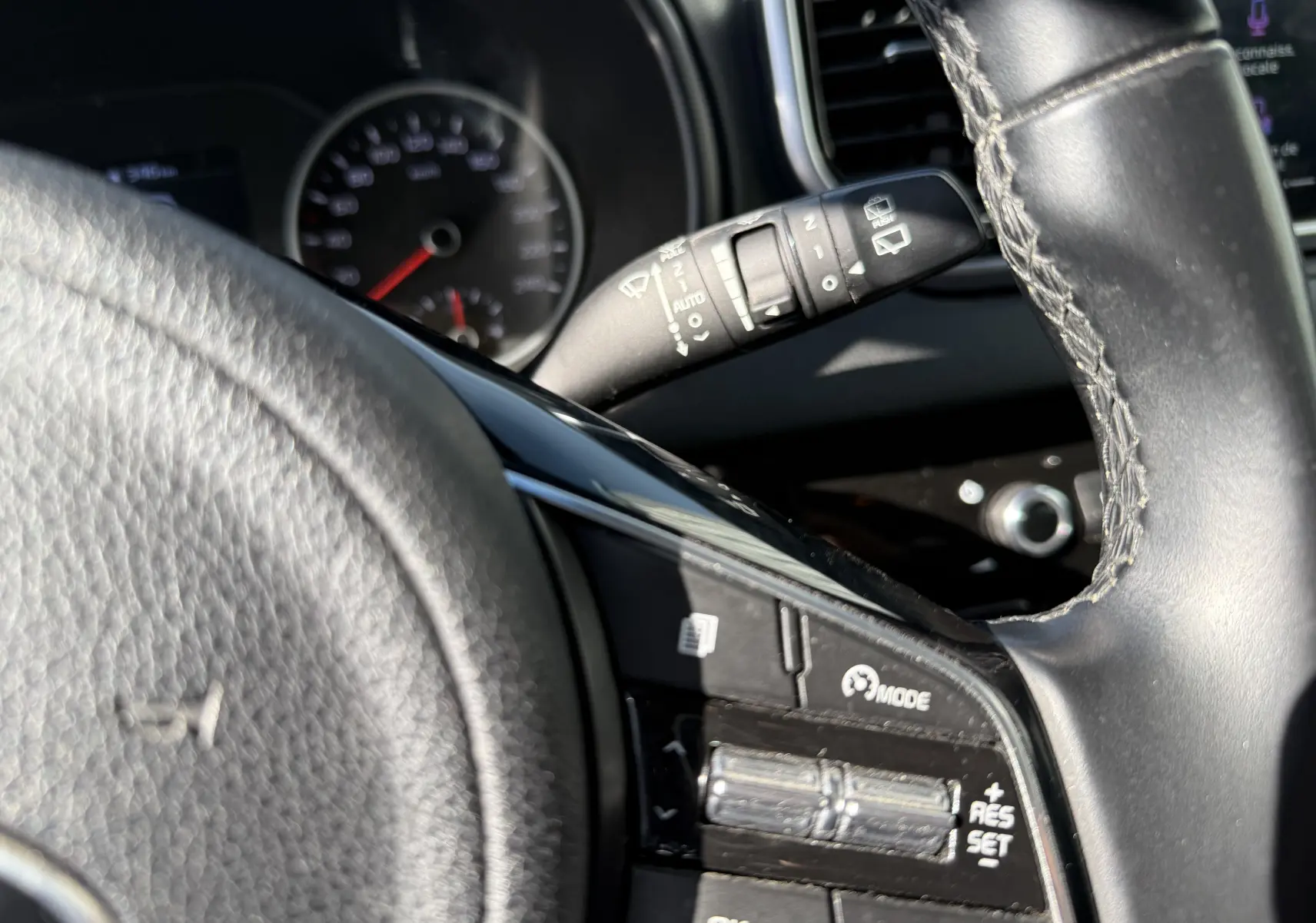 Gros plan sur le volant côté gauche du Kia Sportage bleu 2021, avec commandes de régulateur de vitesse visibles.