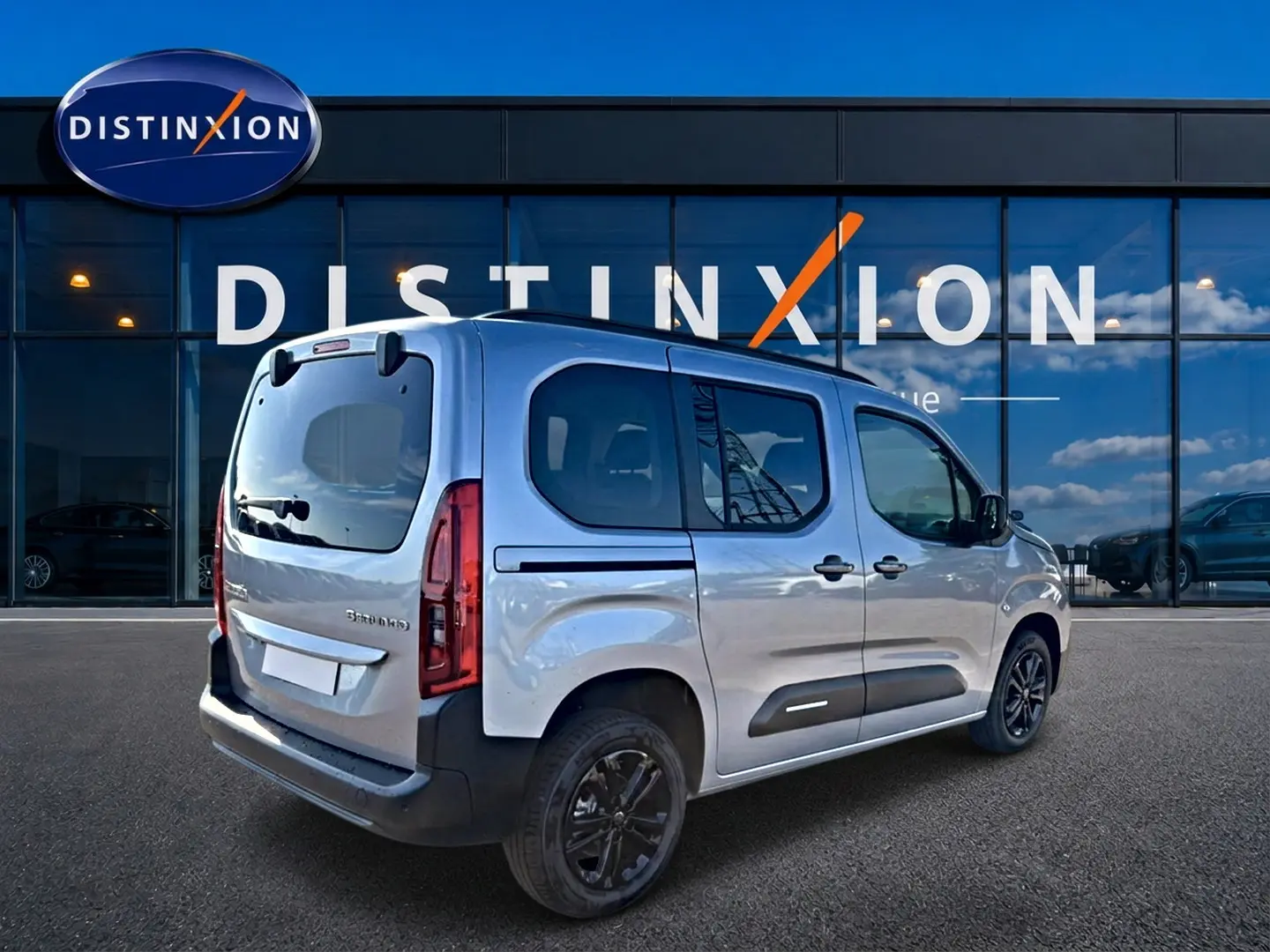 Vue 3/4 arrière droite d'un Citroën Berlingo 2026 gris acier avec barres de toit et jantes alu noires.