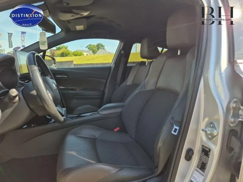 Vue intérieure côté conducteur du Toyota C-HR 122h Distinctive 2019 avec sièges mi-cuir chocolat et volant multifonction.