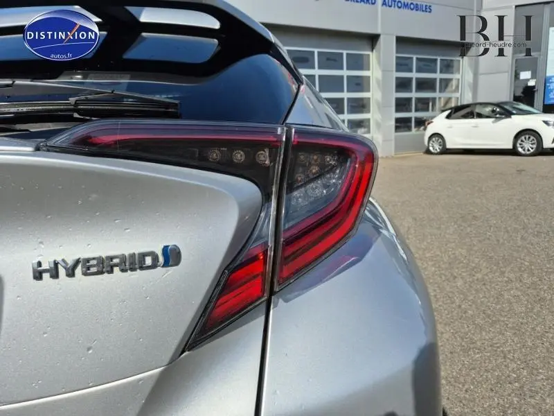 Gros plan sur le feu arrière droit et le logo Hybrid du Toyota C-HR gris aluminium, vue arrière en extérieur.