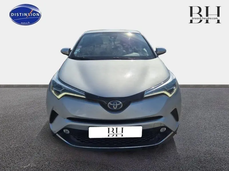 Vue frontale d'un Toyota C-HR 122h Distinctive gris aluminium avec phares LED en forme de flèche et calandre noire.