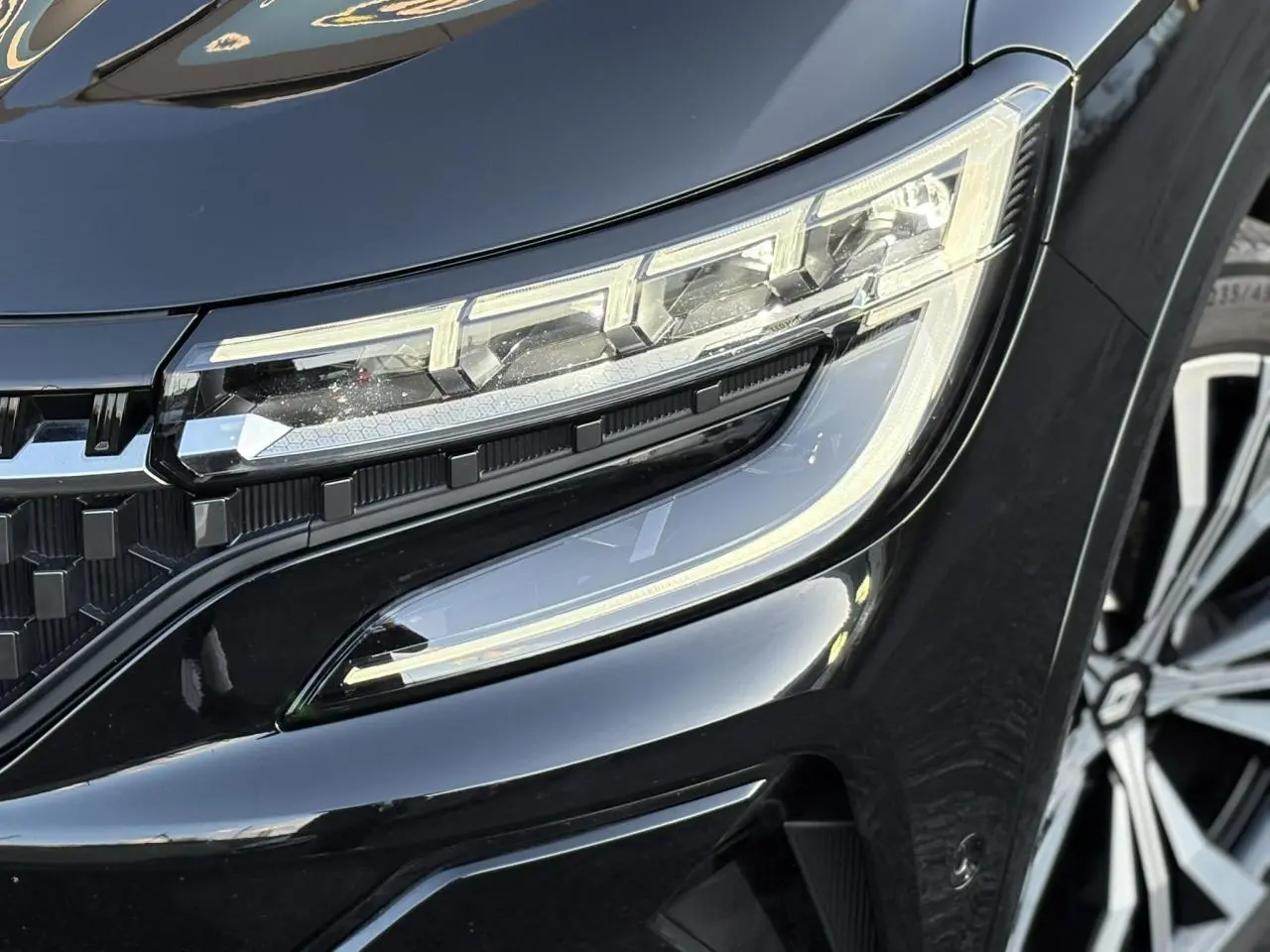 Gros plan sur le phare avant droit et la calandre noire étoilée du Renault Austral 2023 noir Étoile.