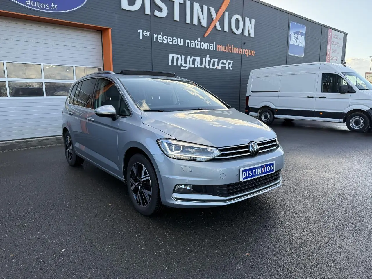 Volkswagen Touran argent Dolomite en 3/4 avant droit, avec jantes alliage et toit ouvrant panoramique visible.