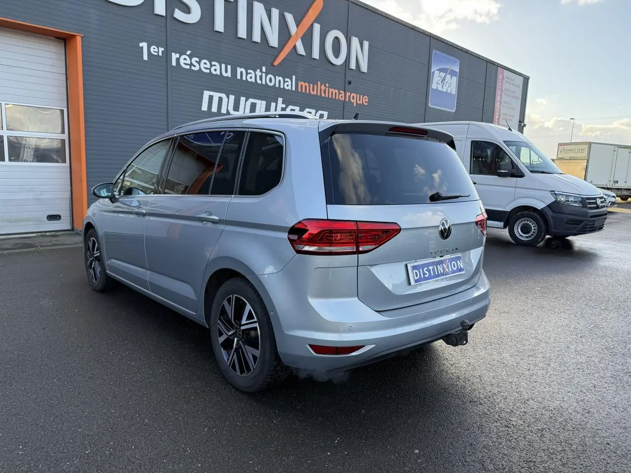 Vue 3/4 arrière droite d'un Volkswagen Touran argent Dolomite avec jantes alliage et attelage visible sur parking.