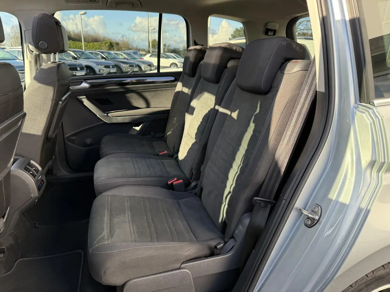 Vue côté droit sur les sièges arrière noirs en microfleece d'un Volkswagen Touran argent Dolomite 2025 avec porte ouverte.