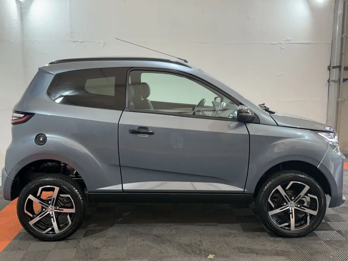 Vue de profil côté gauche de l'AIXAM AMBITION 0.5 CROSSOVER PREMIUM gris foncé avec jantes alliage et caméra rétro côté conducteur.