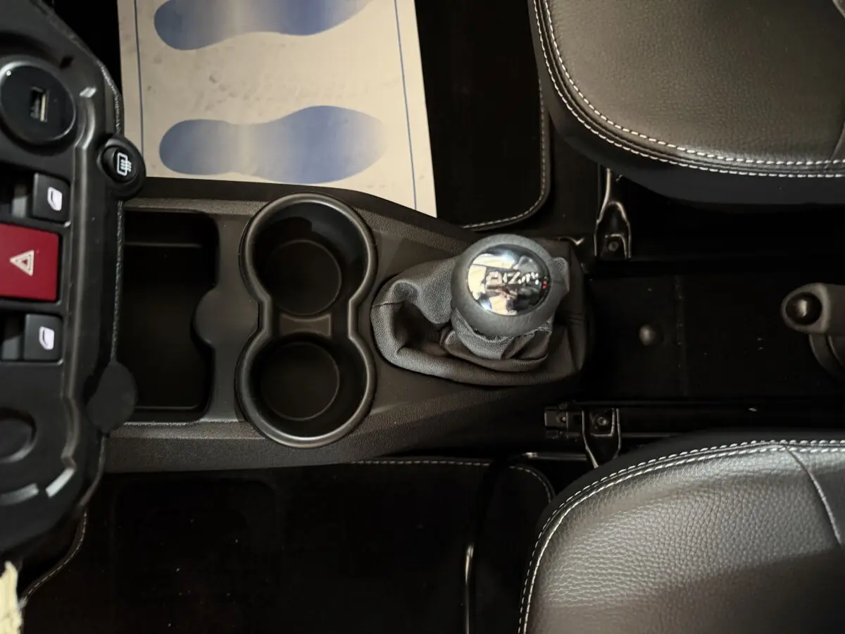 Vue plongeante sur la console centrale de l'AIXAM AMBITION 0.5 CROSSOVER PREMIUM avec levier de vitesse et porte-gobelets noirs.