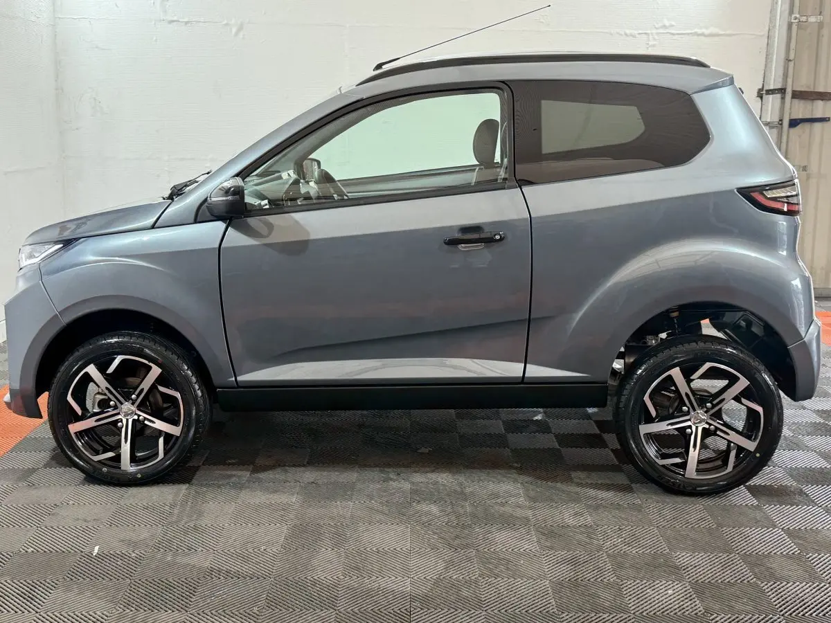 Vue de profil côté gauche d'une Aixam Ambition 0.5 Crossover Premium gris foncé avec rétroviseur caméra côté conducteur.