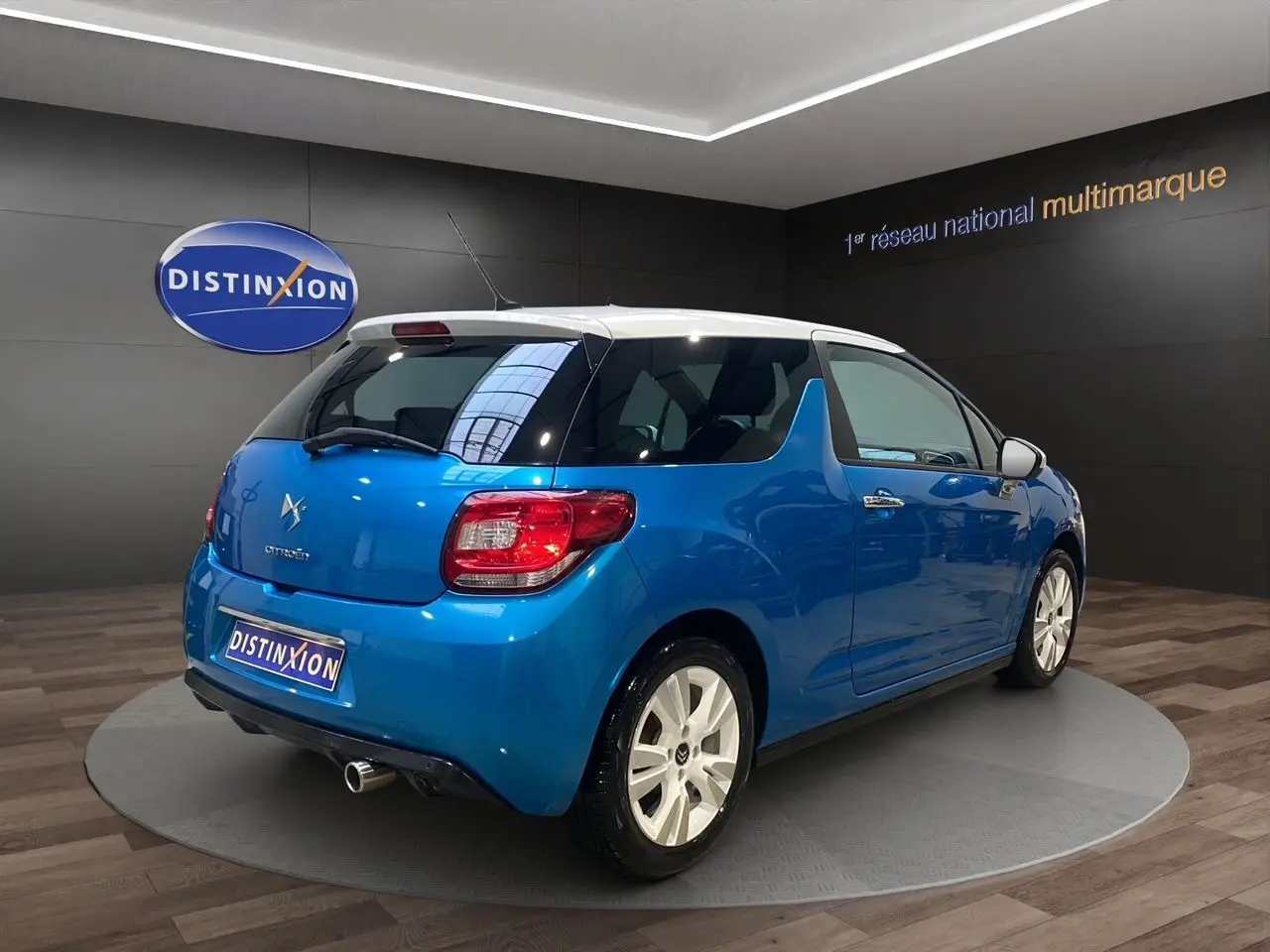 Citroën DS3 bleu avec toit blanc, vue 3/4 arrière droit, sur plateau intérieur avec logo Distinxion.